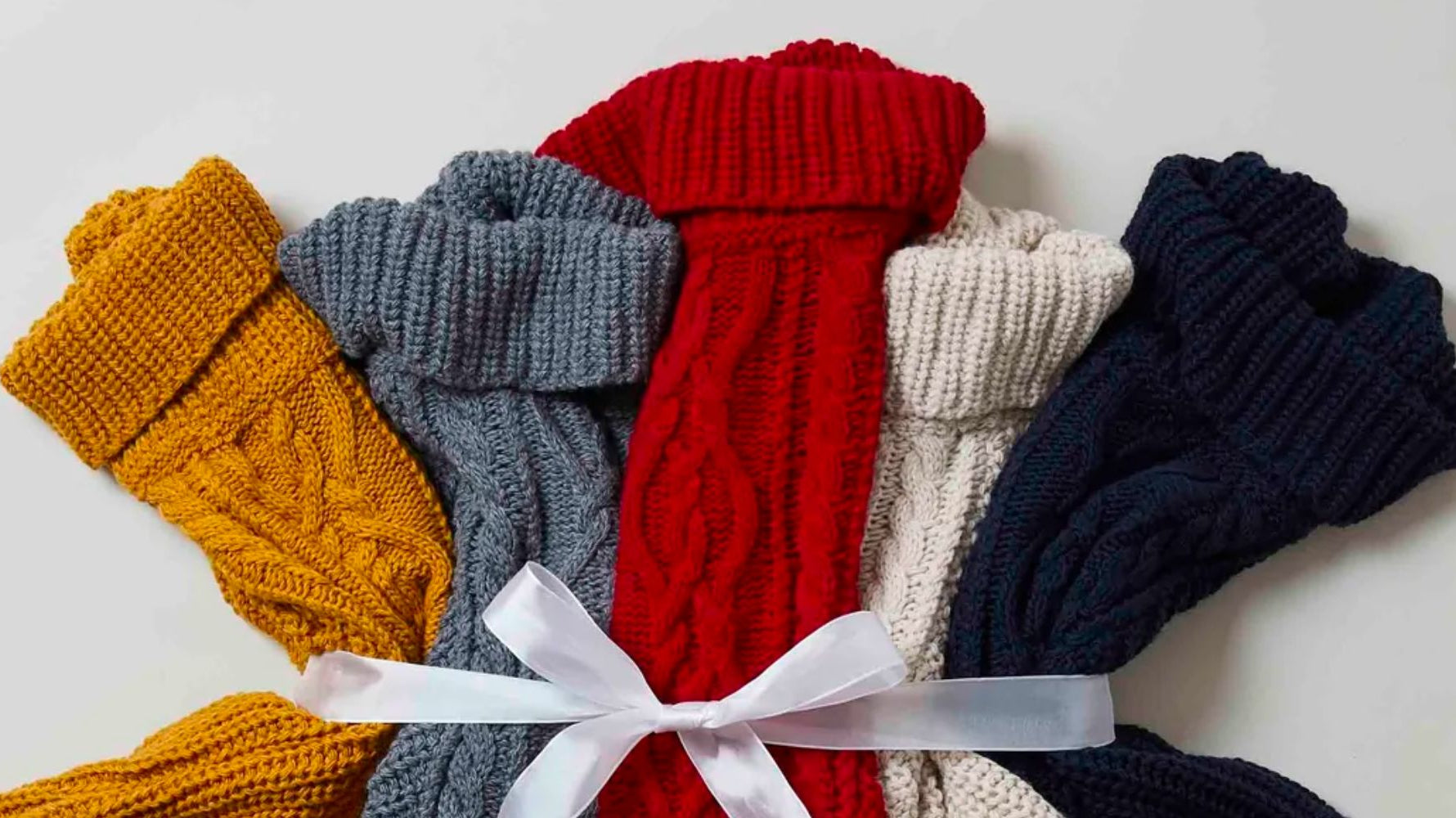 Five knitted ponchos; yellow, grey, red, cream and navy, tied together with a white ribbon