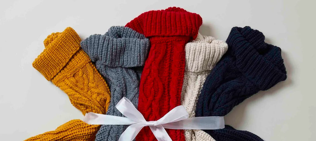 Five knitted ponchos; yellow, grey, red, cream and navy, tied together with a white ribbon